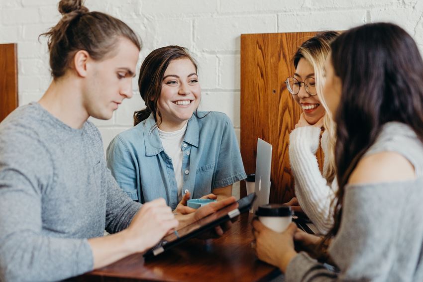 Mennesker som sitter rundt et bord og smiler. Foto: Unsplash