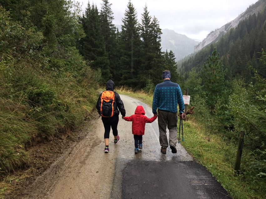 En familie med to voksne og et barn går ute i skogen. De holder hender og vi ser de bakfra. Foto: Alberto Casetta/Unsplash