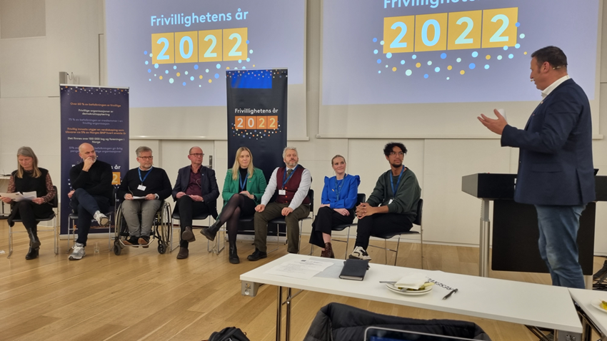 En gruppe mennesker siter i en sal med en ordstyrer.