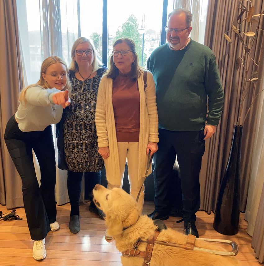 Representanter fra FFO Oslo står foran et vindu. På bildet fra venstre: Robyn Grøndahl peker på kamera, Solveig Magnusson smiler, Synnøve Nordeng smiler, Jørund Schwach ser ned på hunden Milo. I forgrunn er førerhund Milo.